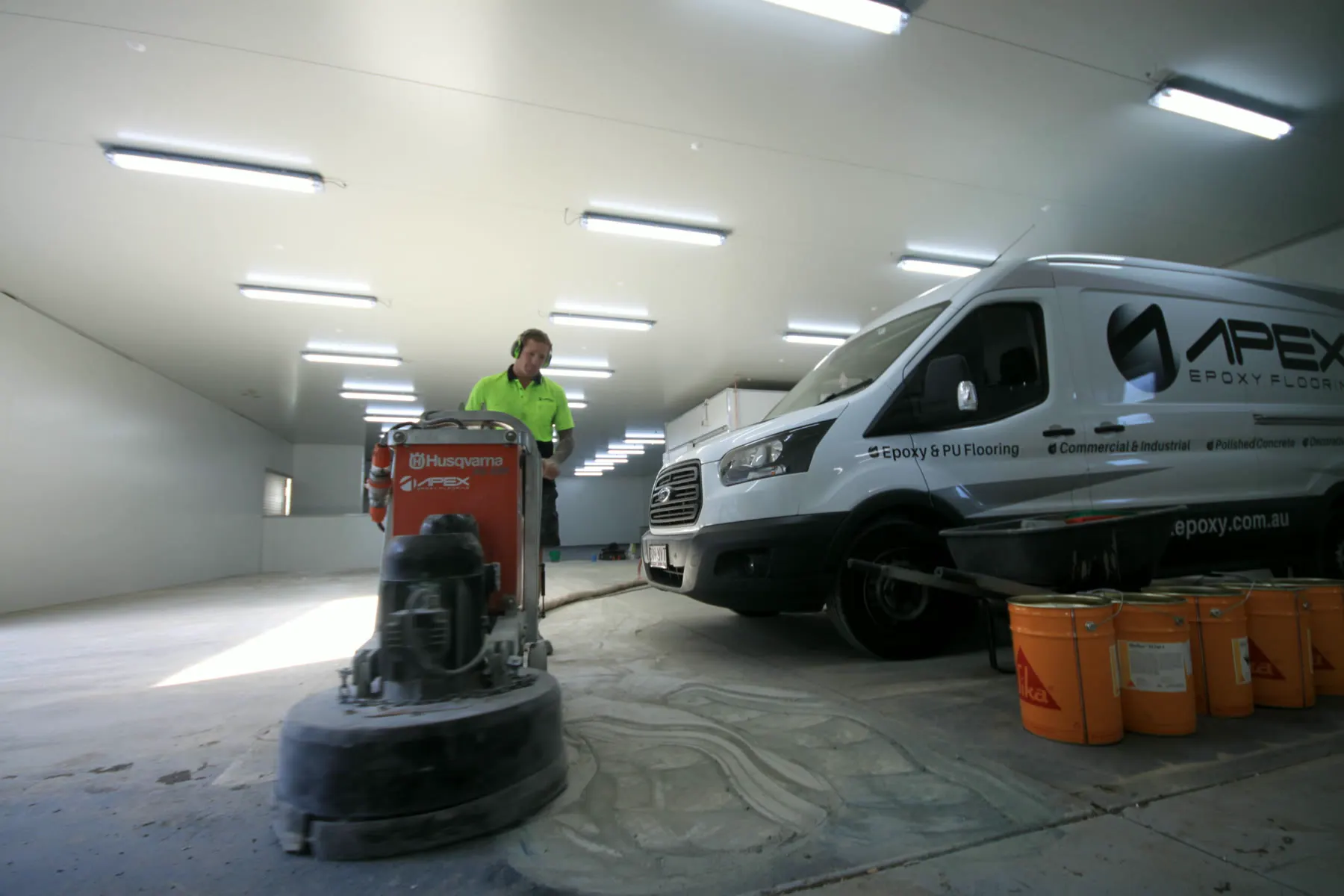 Apex operator grinding a slab beside an Apex Epoxy Flooring van