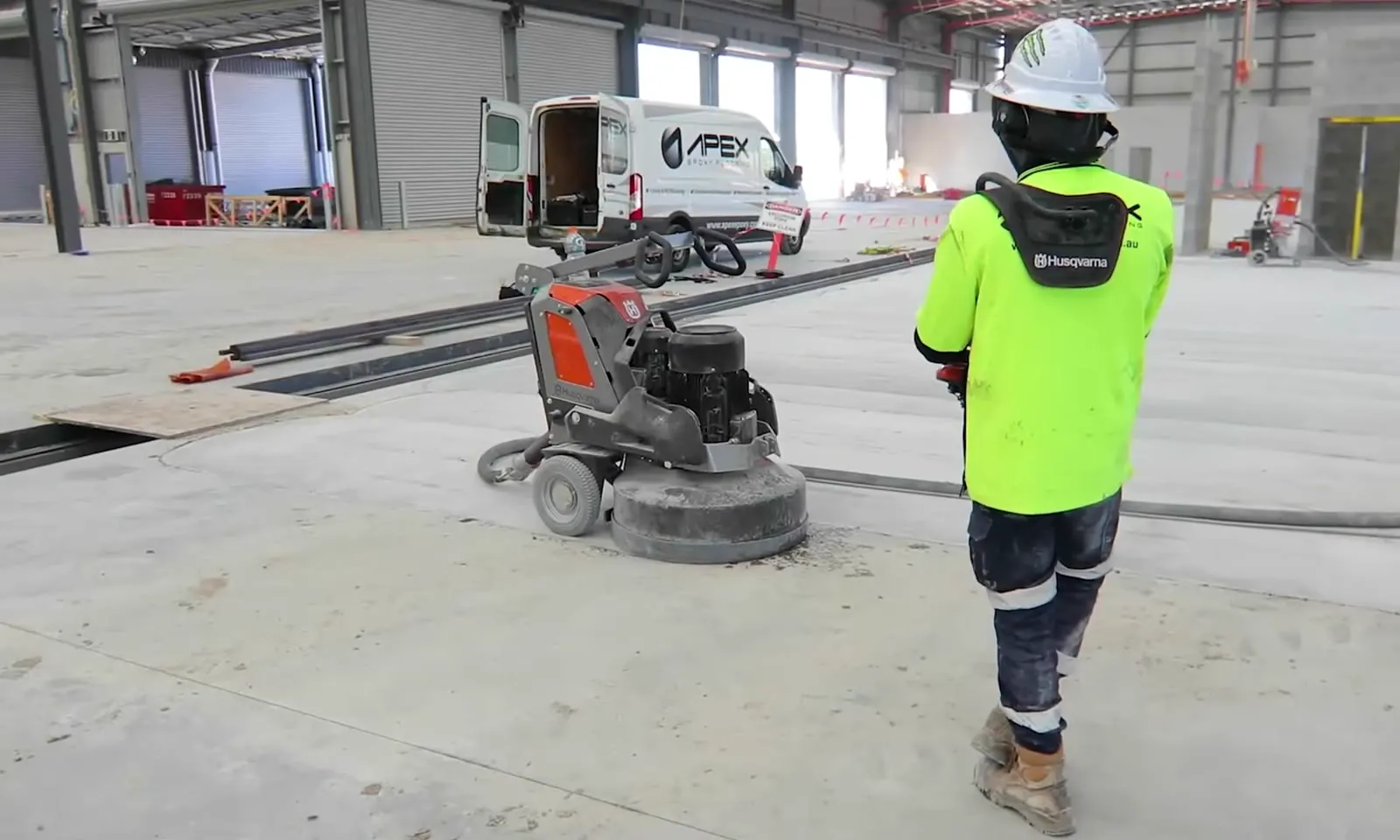 Apex operator walking behind a remote-controlled grinder, with an Apex Epoxy Flooring van behind